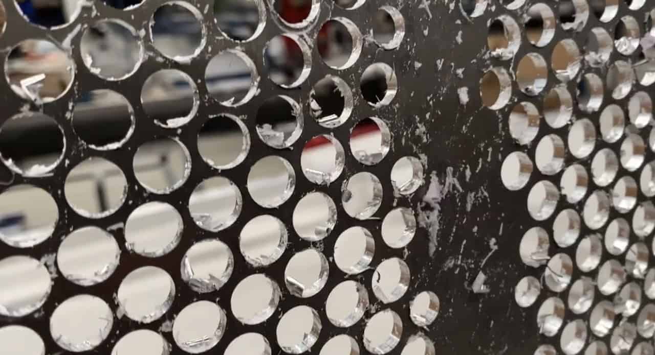 Corrosioned metal surface with circular holes, close-up view.