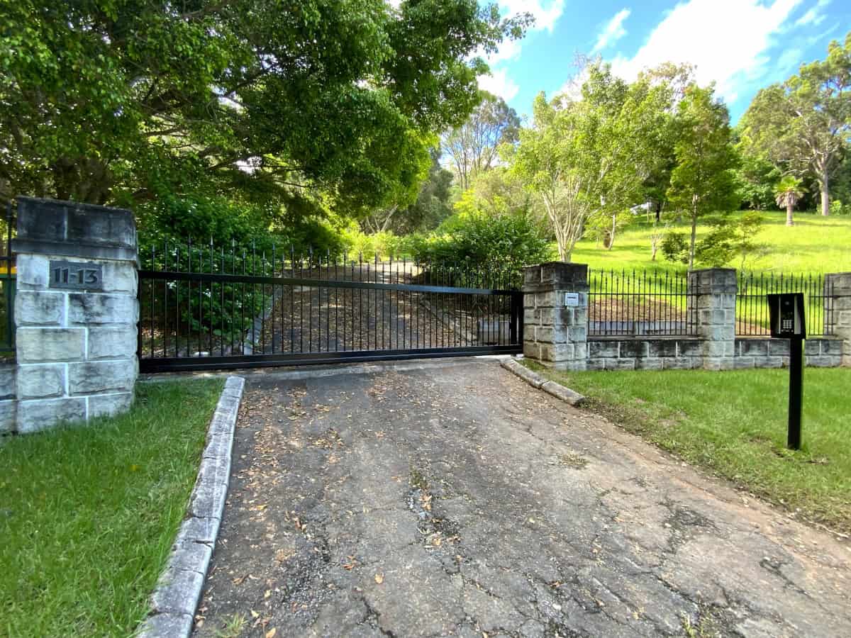 A black steel and aluminium trackless cantilever custom sliding gate installed between two grey brickwork pillars across a driveway