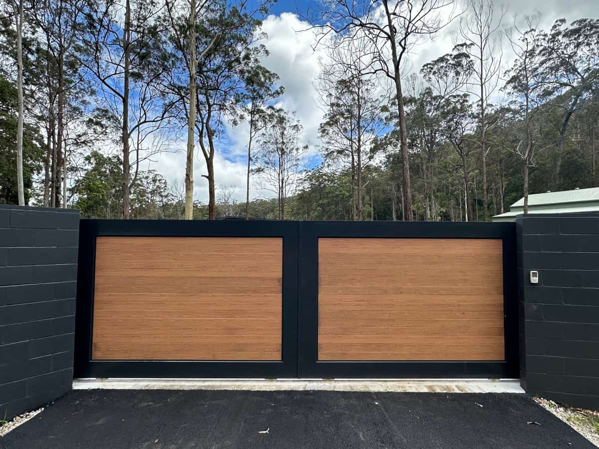A sleek, modern bi-parting sliding gate featuring wood panelling and wall mounted automation controls