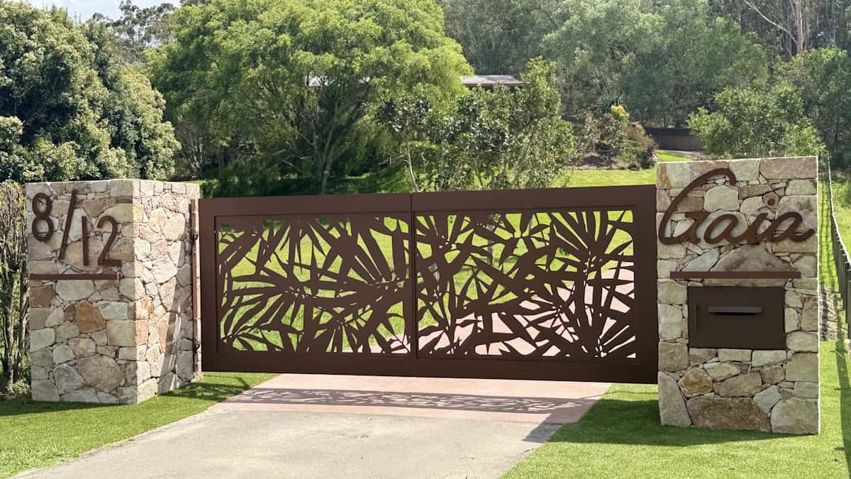 Custom gate design showing intricate leaves, flanked by stone pillars with house numbers and long driveway