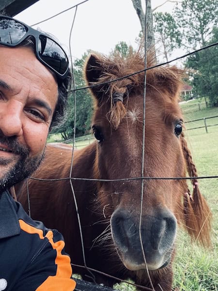 Leo Gkikas, Owner/ Lead Tech, Alpha Gate Automation sharing a selfie with a pony looking over his shoulder through a wire fence