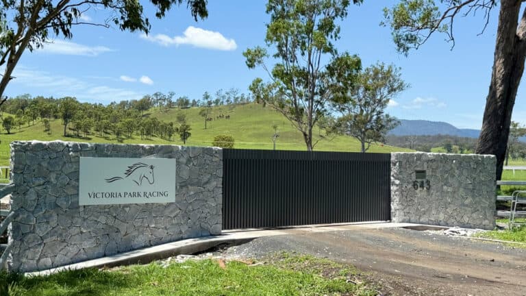 Automatic gate with stone pillars and black slats at Victoria Park Racing premises, scenic natural surroundings, secure entry.